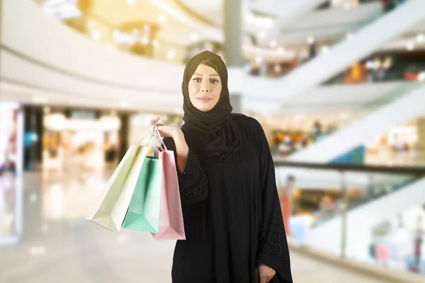 Alışveriş merkezinin koridorunda duran Arap kadın. Arap kadın abaya giyiyor ve alışveriş torbaları tutuyor..