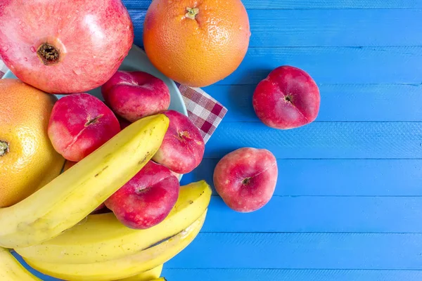 Kırmızı nektarin, muz, plaka ve mavi ahşap zemin üzerine nar