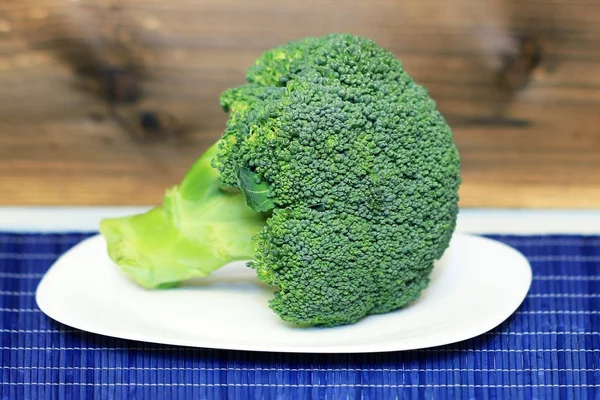 I broccoli freschi giacciono su un piatto bianco. Sfondo in legno. Cibo sano . — Foto Stock