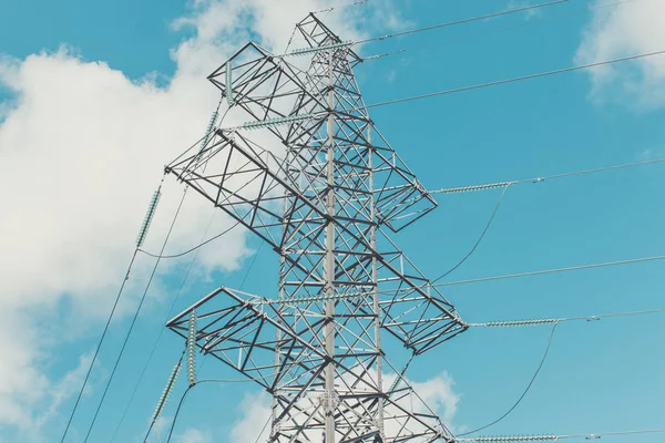 Supports high-voltage power lines against the blue sky with clouds. Electrical industry.