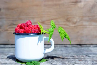 Eski ahşap bir masada olgun ahududu dolu beyaz kupa.