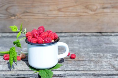 Eski ahşap bir masada olgun ahududu dolu beyaz kupa.