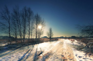 Baharın başında tarlada manzara. Güneşli bir günde eriyen karla dolu kirli bir yol.