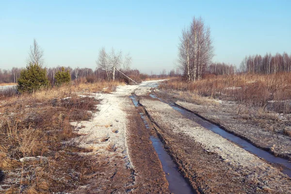 Landschaft im zeitigen Frühling auf dem Feld. Schmutzige Straße mit schmelzendem Schnee an einem sonnigen Tag. — Stockfoto