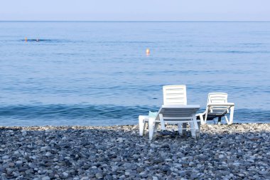 Güneşli bir sabahta iki plastik, beyaz güneşli yatak kıyıda duruyor.