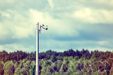 Çit, dikenli tel ve video kamera. Engelleme ve gözetim gözlemi