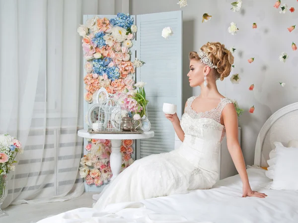 A noiva em um vestido de casamento bebe café no quarto — Fotografia de Stock