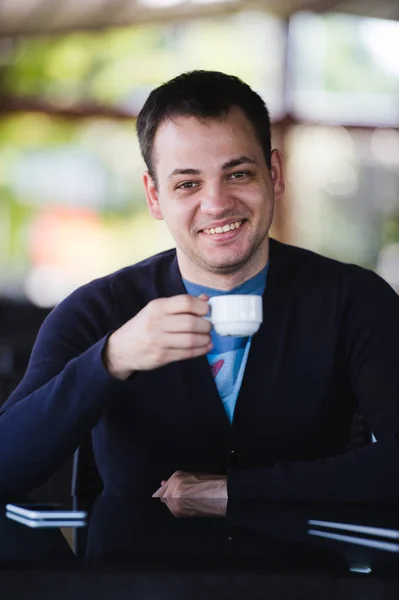 Красивий молодий чоловік працює на ноутбуці і посміхається, насолоджуючись кавою в кафе — стокове фото
