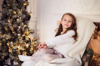 Küçük kız bir battaniye sandalye Noel ağacı sabah evde sarılmış rahat oturan