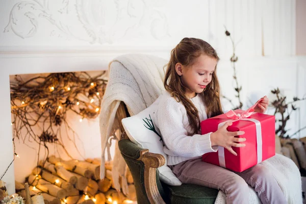 Joyeux enfant fille assise sur un fauteuil recouvert d'une couverture contre la cheminée décorée de Noël — Photo