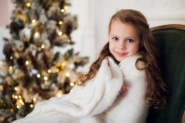 Schattig klein meisje zit door de kerstboom, gewikkeld in een warme deken thuis — Stockfoto