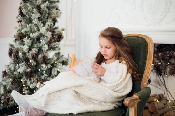 Klein meisje het lezen van boek in de buurt van de kerstboom — Stockfoto