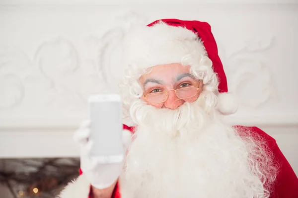 Weihnachtsmann zeigt Smartphone vor rotem Hintergrund — Stockfoto