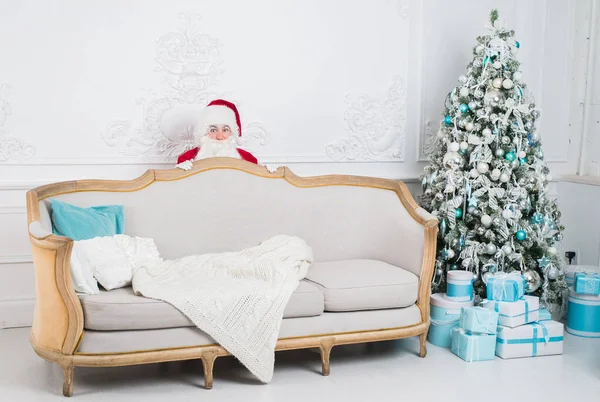 Santa Claus schovává za pohovkou nad domácí interiér — Stock fotografie