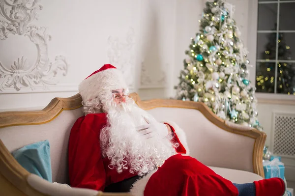 Babbo Natale rilassante sul divano contro l'albero di Natale a casa — Foto Stock