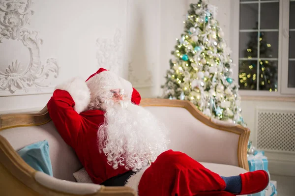 Babbo Natale rilassante sul divano contro l'albero di Natale a casa — Foto Stock