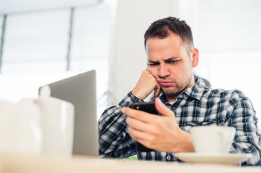 Yorgun yakışıklı genç freelancer kahve dükkanında çalışırken bir cep telefonu kullanarak