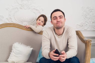telefon ve onunla oynamak isteyen oğlu kullanarak bir kanepede oturan sinirli baba yorgun