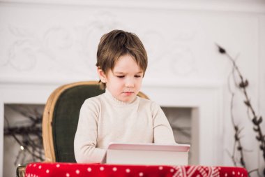 Yeşil sandalyede oturan ve Noel zamanı sırasında bilgisayar tablet ile oynayan sevimli çocuk portresi. Tatil mevsim.
