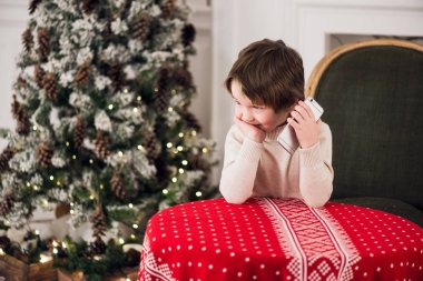 Çocuk Santa oturma sırasında büyük bir yeşil koltukta evde chirstmas üzerinde ağaç arka plan diyor