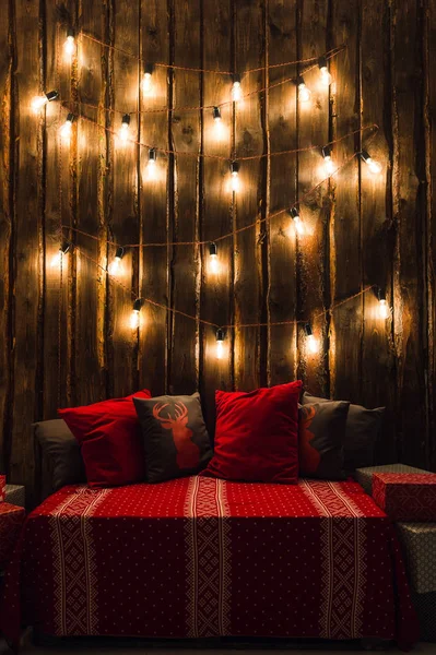 Wooden room in rustic house with  wall and designer light bulbs, decorated place for seat. Red gray pillows. — Stock Photo, Image