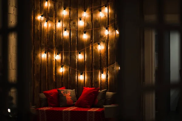 Habitación de madera en casa rústica con pared y bombillas de diseño, lugar decorado para el asiento. Almohadas grises rojas . —  Fotos de Stock