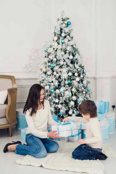 Madre feliz con un niño pequeño cerca del árbol de Navidad. regalos de año nuevo —  Fotos de Stock