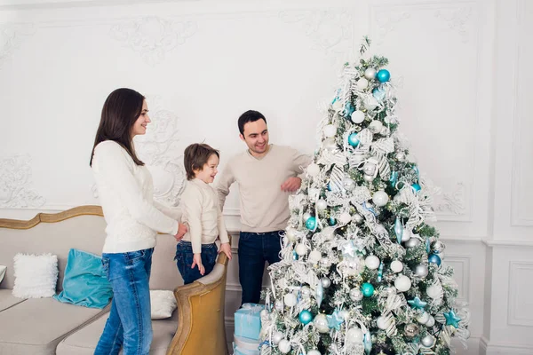 La alegre pareja casada está celebrando la Navidad con su hijo. Están decorando abeto y riéndose —  Fotos de Stock
