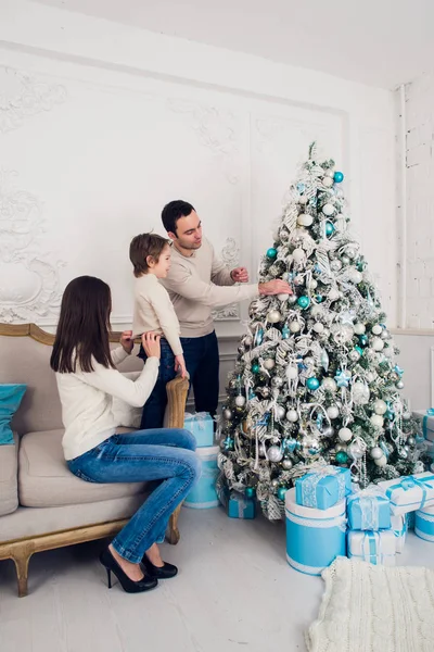 La alegre pareja casada está celebrando la Navidad con su hijo. Están decorando abeto y riéndose —  Fotos de Stock