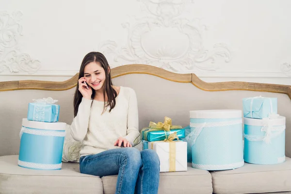Trendi fiatal nő ül a kanapén, a karácsonyi ajándékokat beszél vele mobiltelefon — Stock Fotó