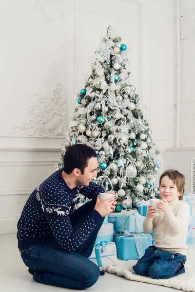 Feliz padre e hijo con tazas de té hablando cerca de Navidad en casa —  Fotos de Stock