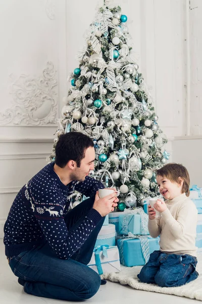 Feliz padre e hijo con tazas de té hablando cerca de Navidad en casa —  Fotos de Stock