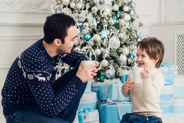 Feliz pai e filho com xícaras de chá falando perto da hora de Natal em casa — Fotografia de Stock