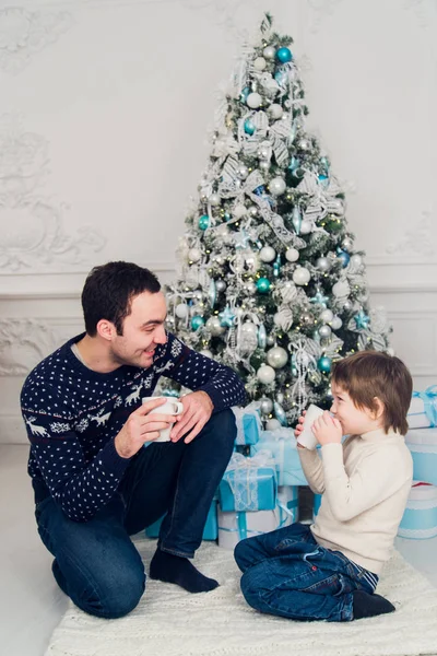 Gelukkig vader en zoon met kopjes thee praten in de buurt van Kerstmis thuis — Stockfoto