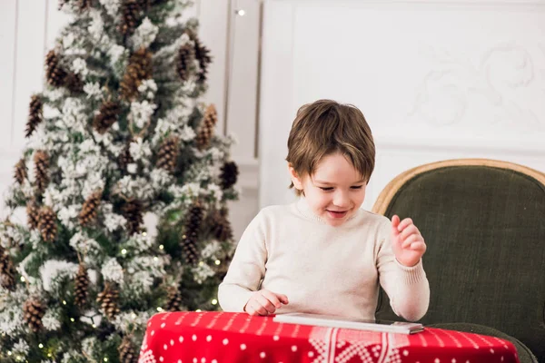 Yeşil sandalyede oturan ve Noel zamanı sırasında bilgisayar tablet ile oynayan sevimli çocuk portresi. Tatil mevsim.