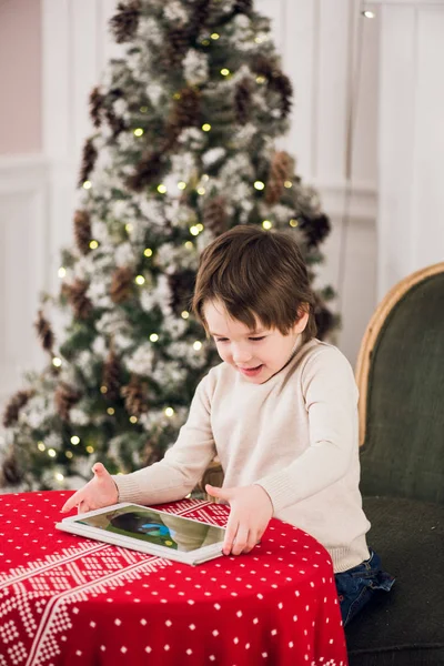 Yeşil sandalyede oturan ve Noel zamanı sırasında bilgisayar tablet ile oynayan sevimli çocuk portresi. Tatil mevsim.