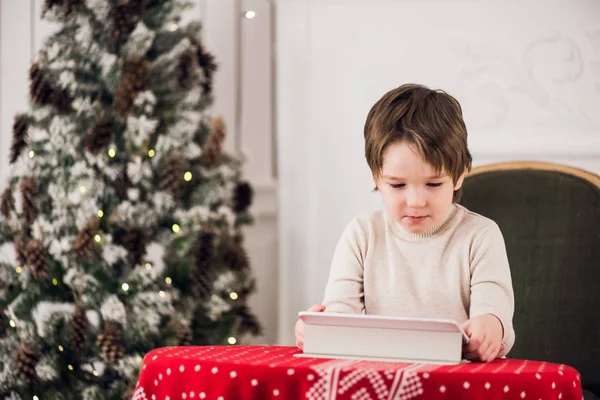 Portret van schattige jongen jongen op groene stoel zitten en spelen met computer tablet tijdens de kerstperiode. Vakantie seizoenen. — Stockfoto