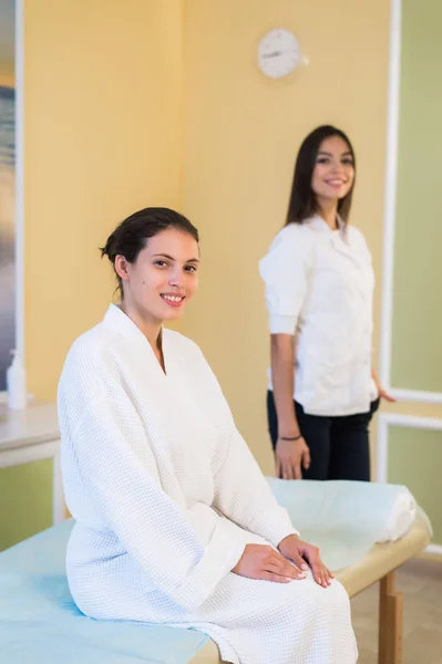 Médico esteticista mujer con paciente en centro de bienestar spa. Joven cosmetóloga profesional hacer masaje de cuello a hermosa chica morena en el gabinete de cosmetología o salón de belleza . — Foto de Stock