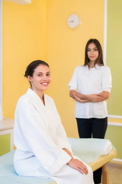 Médico esteticista mujer con paciente en centro de bienestar spa. Joven cosmetóloga profesional hacer masaje de cuello a hermosa chica morena en el gabinete de cosmetología o salón de belleza . —  Fotos de Stock