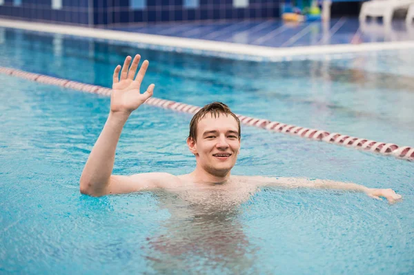 Joven hombre feliz en la piscina con una mano arriba animando — Foto de Stock