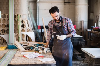 Bir marangoz ahşap stüdyosunda ayakta ve dijital tablet tutan portresi