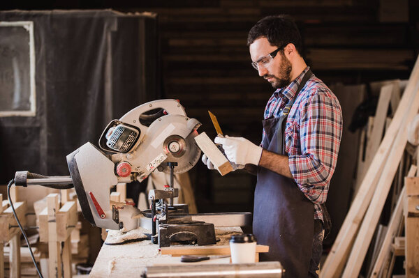 profession, carpentry, woodwork people concept - carpenter with wood plank and notebook checking his notes at workshop