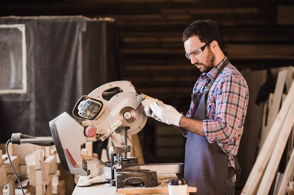 Les rêves naissent dans mon atelier. Jeune menuisier homme confiant tenant une planche de bois debout dans sa menuiserie — Photo