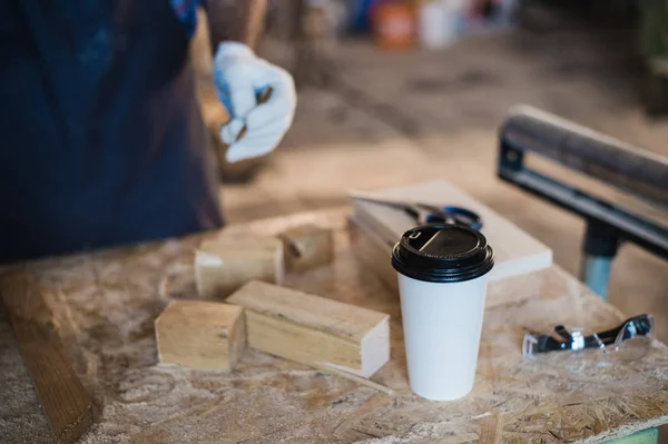 Moderno lugar de trabajo de carpintería con tableta, café, tijeras y piezas de madera en la mesa, en el taller —  Fotos de Stock