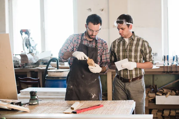 Feliz carpintero masculino mostrando algo a su compañero de trabajo en sus cuadernos en el taller — Foto de Stock