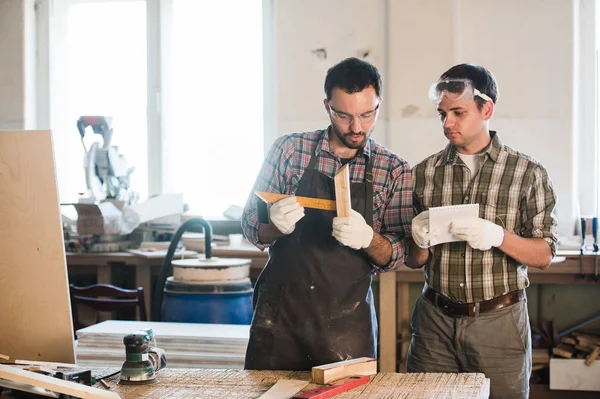 Heureux charpentier masculin montrant quelque chose à collègue à ses papiers de cahier dans l'atelier — Photo