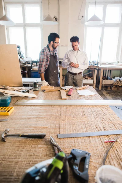 Feliz carpintero masculino mostrando algo a su compañero de trabajo en sus cuadernos en el taller — Foto de Stock