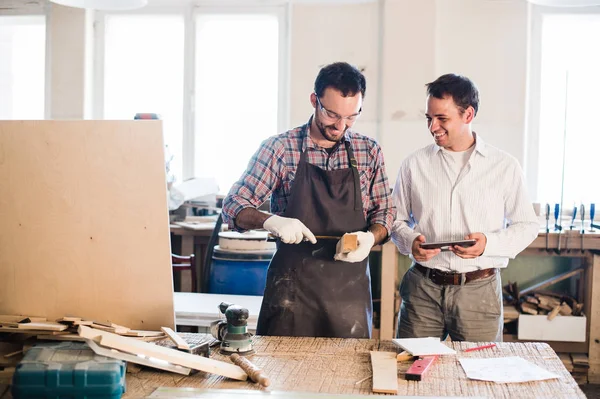 Heureux charpentier masculin montrant quelque chose à collègue à ses papiers de cahier dans l'atelier — Photo