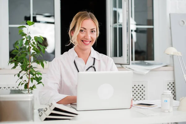 Retrato de la joven y feliz doctora trabajando en la computadora en su oficina —  Fotos de Stock