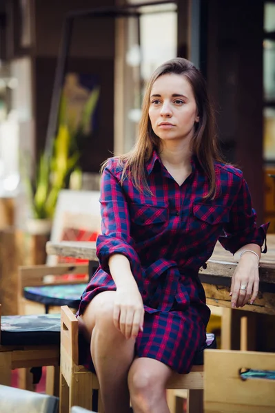 Ovan Visa vacker kvinna i violett rutig klänning sitter vid bord på terrassen i cafeterian. Hon ser att kameran — Stockfoto